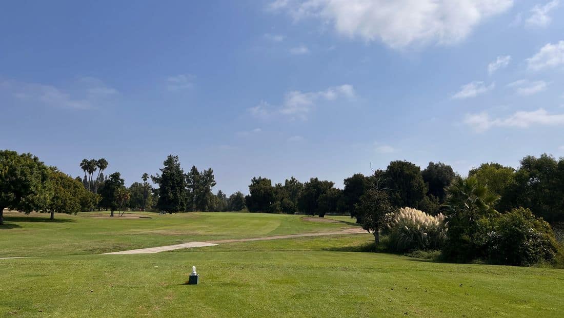 A broad fairway framed by trees beneath a blue sky