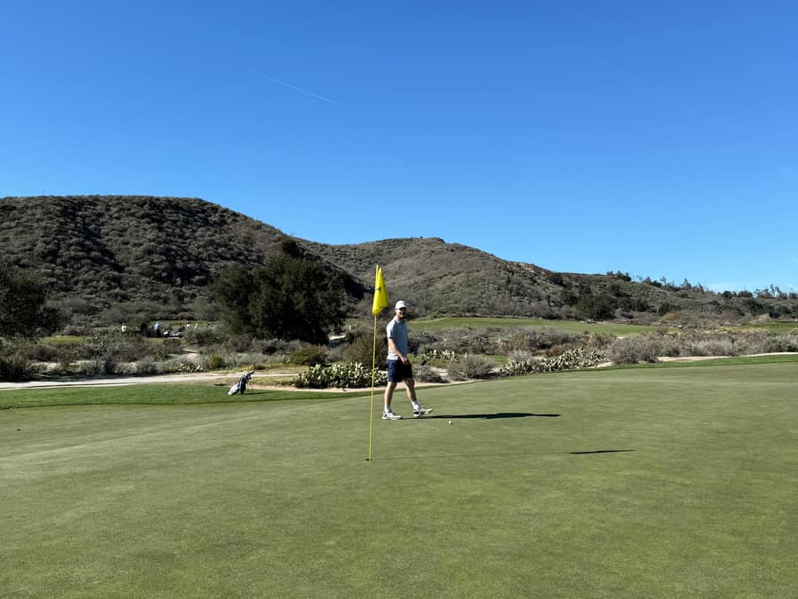 A golfer holding a flag on a green below dry hills