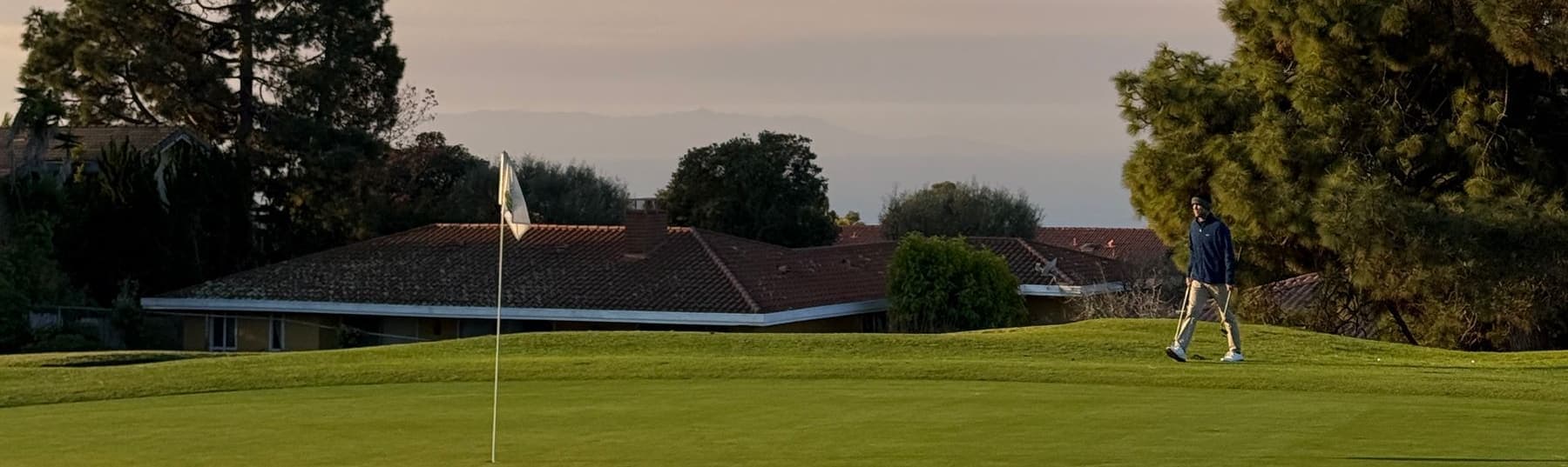 A golfer walking across a green in low evening light